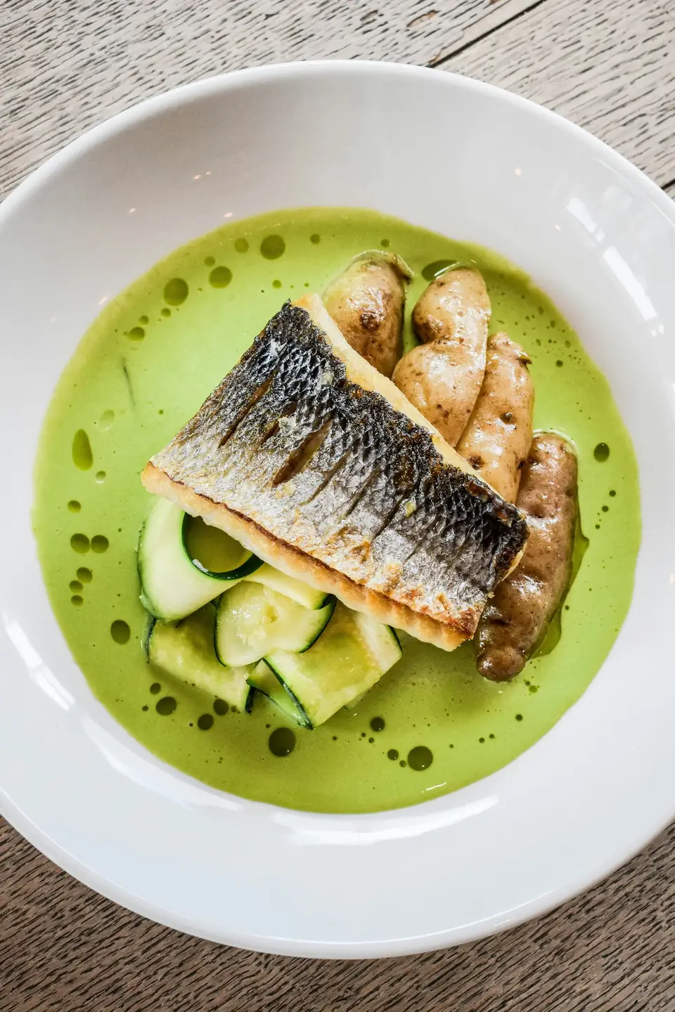 Filet de poisson à la peau dorée posé sur une sauce verte, avec des pommes de terre et du concombre