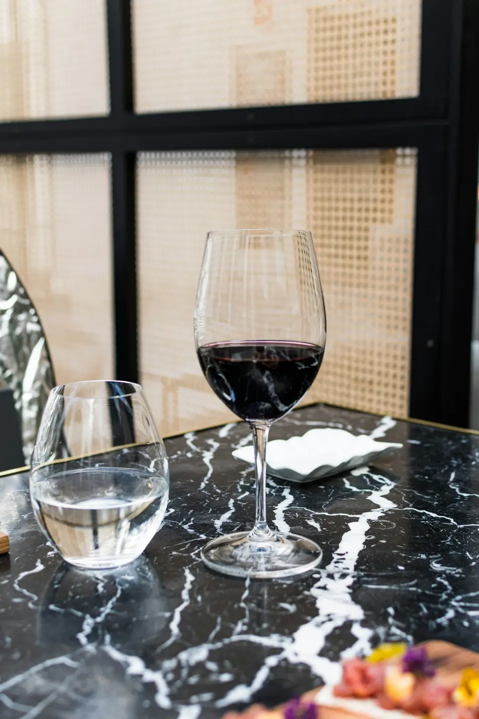Verre de vin rouge posé sur une table en marbre noir, devant une cloison en cannage